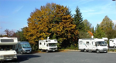 Wohnmobilparkplatz mit mehreren Wohnmobilen, umgeben von Bäumen und Grünfläche
