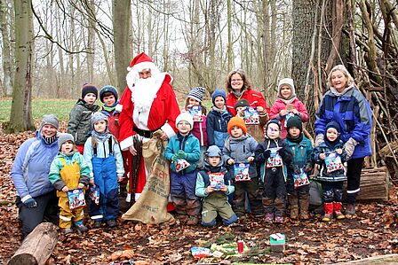 14 Kinder und 3 Erzieherinnen mit dem Nikolaus im Wald. Die Kinder haben eine Tüte Süßigkeiten in der Hand.