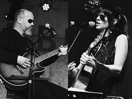 Ein Mann und eine Frau spielen Gitarre und die Frau singt. 
