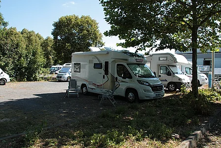 Wohnmobile auf dem Wohnmobilparkplatz am Schwimmbad. Wohnmobile stehen im Schaten unter Bäumen.