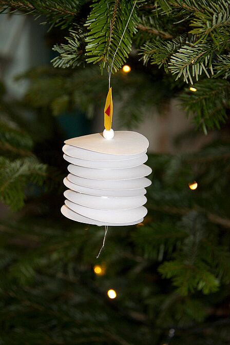 weiße Papierkerze hängt an einem Ast von einer Tanne